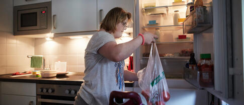 Eine Frau mit Down Syndrom räumt ihre Einkäufe in den Kühlschrank.