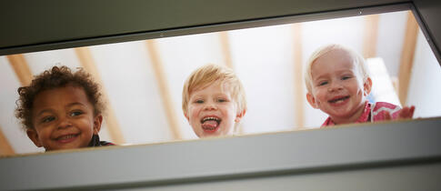 Drei Kinder schauen durch ein Fenster und lachen. 