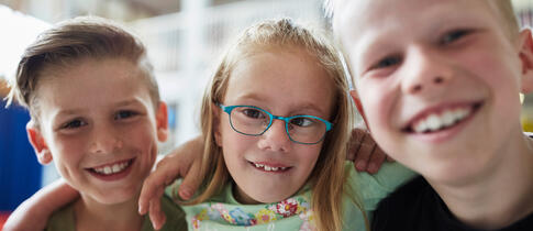 Drei Kinder liegen in den Armen und lachen in die Kamera